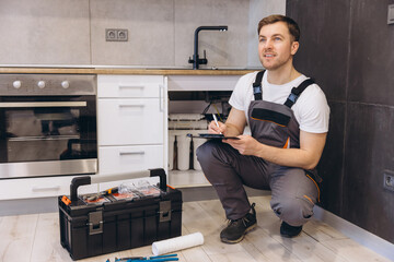 Plumber Inspecting Pipes and Taking Notes in Kitchen
