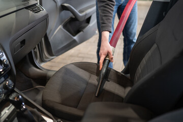 A man uses a vacuum cleaner and cloth to clean the dashboard of a car at a car wash. For automotive maintenance, cleaning services, and interior care content.