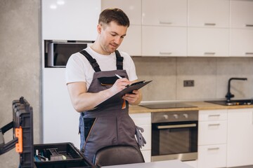 Plumber writing notes on clipboard in kitchen