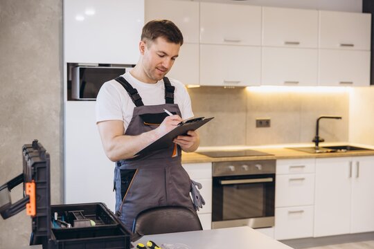 Plumber writing notes on clipboard in kitchen