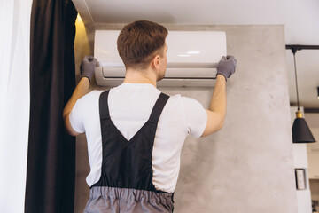 Professional plumber installing modern air conditioner unit on wall