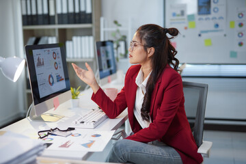 Young Asian businesswoman discussing marketing data on computer screen with colleagues during a meeting in the office