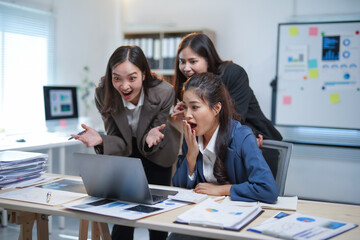 Three asian businesswomen are looking surprised and excited at their laptop in the office, celebrating a successful business achievement