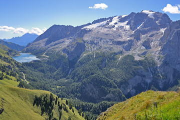 Fototapeta premium Sunny panorama mountain landscape with Marmolada glacier against blue sky, during a hike on the popular Bindelweg. Dolomites (Dolomiti), Italy. Left background the lake Lago di Fedaia reservoir.