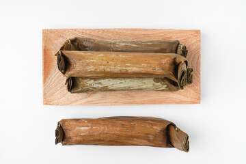 Fototapeta premium Lontong or rice cake on wooden plate. Traditional Javanese food made from steamed rice and wrapped in banana leaves. Isolated on white background, flat lay setup