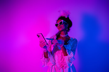 Elegant young woman in lace gown holding phone against neon pink and purple backdrop