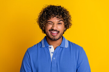 Delighted young man winking playfully against bright yellow background, exuding confidence and joy...