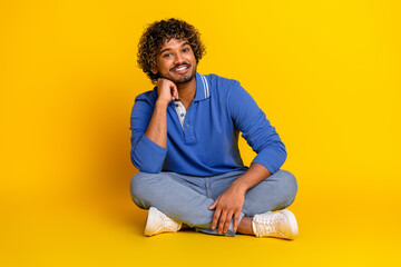 Portrait of a cheerful young man sitting on a yellow background, wearing a blue polo, showcasing...