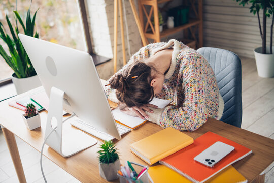Young woman resting her head on desk while working at home during daylight hours, surrounded by a comfortable and stylish living space.