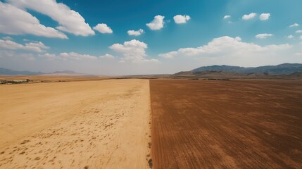 Fototapeta premium Aerial view of vast desert landscape with contrasting sandy areas. Blue sky, white clouds, and distant mountains under sunny weather.