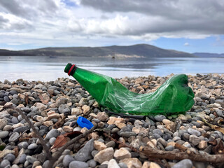 A crumpled plastic bottle and cap lie on a public pebble beach, plastic contamination