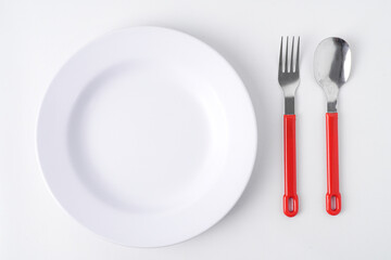 Empty white colored round shaped plate, red handle spoon and fork. Isolated on white background. Flat Lay Setup