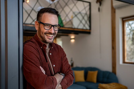 Happy architect smiling with arms crossed, enjoying his modern designed tiny house