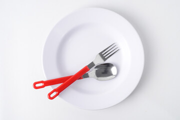 Empty white colored round shaped plate, red handle spoon and fork. Isolated on white background. Flat Lay Setup