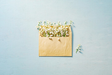 Lilies of the valley clustered inside a postal envelope on blue wooden surface. © Mr. Music