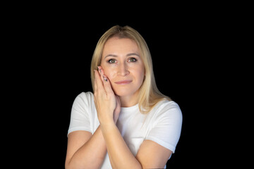 Fototapeta premium Close up of woman has a toothache, touches her teeth and frowns from painful discomfort, stands over black background.