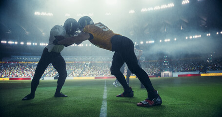 American Football Players Compete on Stadium, Illuminated by Bright Lights With a Cheering Sports Crowd in the Background. Strong Athletes Play an Intensive Dynamic Game Under Heavy Rain