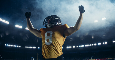 Athletic American Football Player Standing in Uniform in the Middle of the Field, Celebrating a Triumphant Championship Winning Game. Fans Cheering From Their Stadium Seats © Gorodenkoff