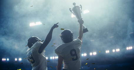 American Football Team Celebrating a Championship Victory with Trophy and Falling Confetti Under Stadium Lights. Emotional Moment of Triumph for Two Diverse Footballers in White Jerseys