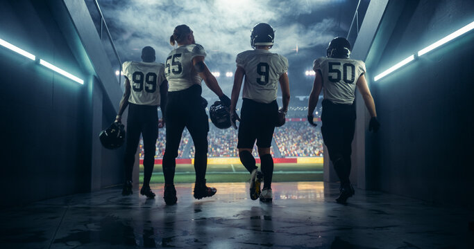 American Football Players Walk Out of Stadium Tunnel for Championship Game, Entering the Field with Determination and Unity, Ready to Compete and Win. High Energy Atmosphere in a Packed Stadium - Powered by Adobe