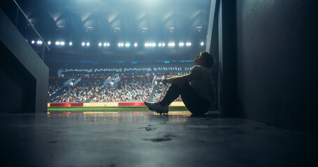 Tired American Football Player Sitting Alone in Stadium Tunnel, Helmet on Ground. Emotional Male Athlete Reflecting on a Failed Game, Coping with a Defeat, Showing Resilience After Championship Game