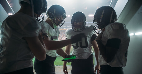 American Football Players Using Tablet to Go Over Game Strategy Before Walking on Stadium Filled with Energetic Sports Fans and Team Supporters. Multiethnic Footballers Getting Ready