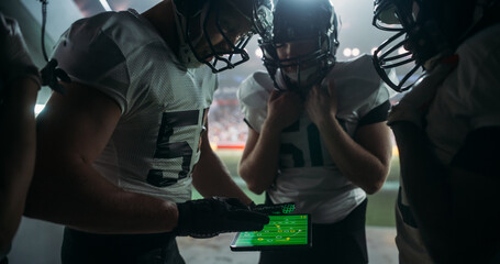 American Football Players Using Tablet Computer to Go Over Game Strategy Before Walking on a Stadium Filled with Energetic Sports Fans and Team Supporters. Multiethnic Footballers Getting Ready