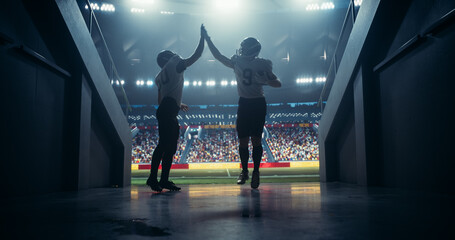 Two Professional American Football Players Exit the Stadium After a Competitive Game of Gridiron. Exhausted but Happy Footballers are Cheered by a Full Arena of Sports Fans in a Stadium with Lights