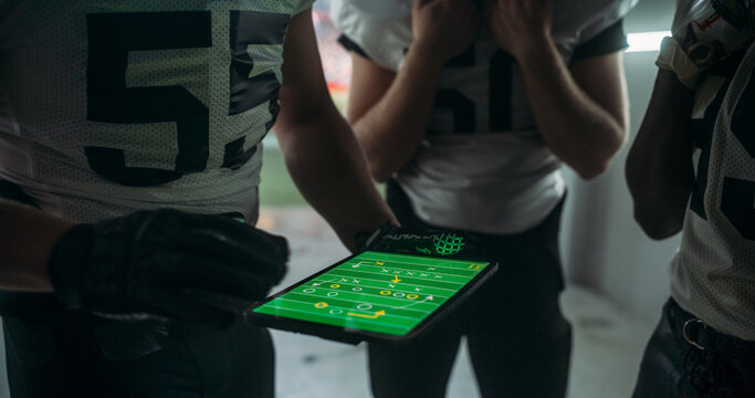 Football Stadium Tunnel: Group of Athletic American Football Players Planning Game Strategy on a Tablet Computer Before Championship Match. Crowd of Spectators Cheering in the Background