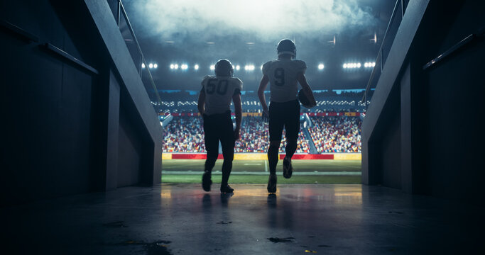 Diverse Professional American Football Players Running Out of the Stadium Tunnel Together. Football Players are Welcomed by a Full Arena of Sports Fans in a Big Outdoors Stadium