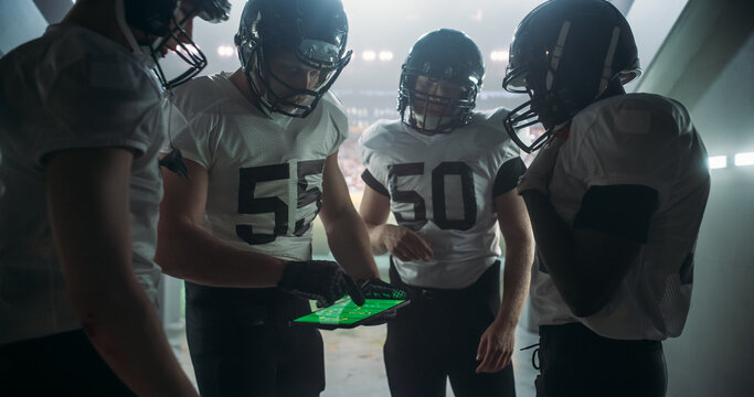 American Football Players Using Tablet Computer to Go Over Game Strategy Before Walking on Stadium Filled with Energetic Sports Fans and Team Supporters. Multiethnic Footballers Getting Ready - Powered by Adobe