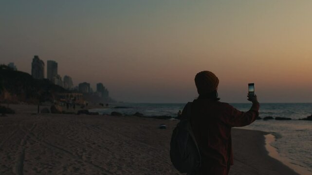 Travel to Israel. Girl takes photos of the city and the beach on her phone for social networks. Sunset on the beach. beach in Netanya. Travel and content creation. Netanya. Israel.