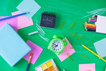 Back to school concept. School supplies and alarm clock on green background, with copy space, top view.