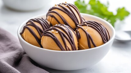 A bowl of creamy dessert features four scoops drizzled with rich chocolate, showcasing a delicious treat perfect for indulgence.