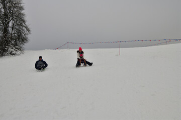 Family tobogganing down a snowy hill during winter vacation