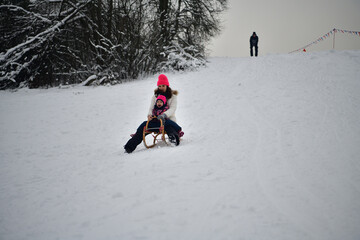 Two girls are tobogganing downhill on snowy hill in winter 