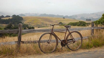 Fototapeta premium A countryside landscape featuring an old-fashioned bicycle leaning against a wooden fence, with rolling green hills in the background.