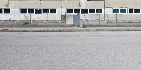 Green metal wire mesh with an utilities box in the middle. Industrial building with a long row of...