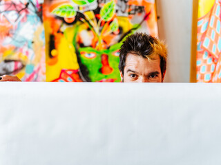 Artist Peeking Over a Blank Canvas in His Studio. An Argentine artist playfully peeks over a blank...