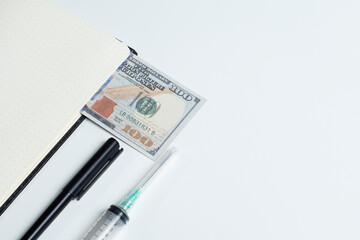 Creative flatlay of doctor medical equipment, white table with books, dollar bills, syringe and black pen. Health care cost concept, Top view with copy space, Isolated on white.