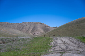 Das Bild zeigt eine weite, trockene Landschaft unter strahlend blauem Himmel. Ein Feldweg durchschneidet den Vordergrund und f&uuml;hrt zu einer fernen Bergkette. 