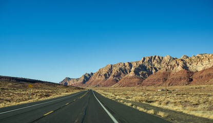 Das Bild f&auml;ngt eine weite W&uuml;stenlandschaft ein, in der ein einsamer Highway unter strahlend blauem Himmel durch ein zerkl&uuml;ftetes Gel&auml;nde f&uuml;hrt.