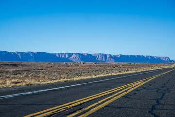 Das Bild zeigt eine weitl&auml;ufige Autobahn, die sich durch eine w&uuml;sten&auml;hnliche Landschaft schl&auml;ngelt. Der Himmelist klar und blau und bietet einen sch&ouml;nen Kontrast zu den erdigen T&ouml;nen der W&uuml;ste. 