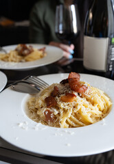 A plate of closeup carbonara spaghetti topped with grilled bacon with red wine in background. It is an Italian pasta dish from Rome made with egg, hard grated cheese, cured pork 
