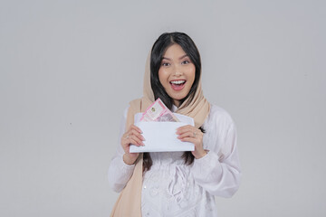 Fototapeta premium Excited Asian Muslim pregnant woman in a veil hijab holding Eid Al Fitr money gift or THR.