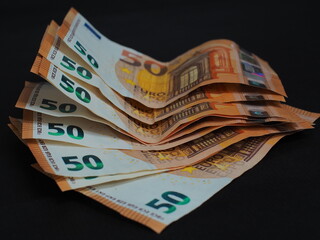 Multicolored 50 euro bills are neatly stacked on a black background. Numbers and security features are clearly visible