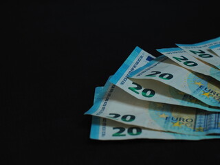 20 Euro bills are arranged in a fan on a black background. Design elements, denominations and...