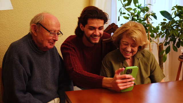 Grandparents and grandson laughing and using smartphone at home - Powered by Adobe