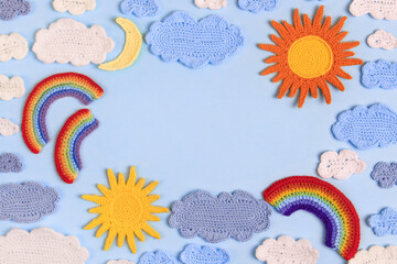 Knitted toys blue and white clouds, yellow sun, rainbow, moon on blue background. Baby stuff and accessories. Top view, flat lay