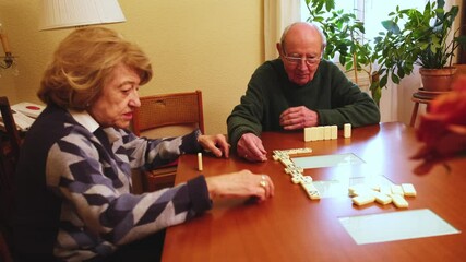 Elderly couple playing dominoes on a wooden table in their living room, enjoying their free time together - Powered by Adobe